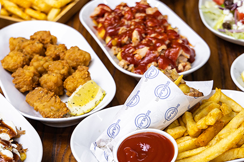 Assortments of plates and bowls with different greek food on each, including chips, HSP, souvlaki, sauce and calamari