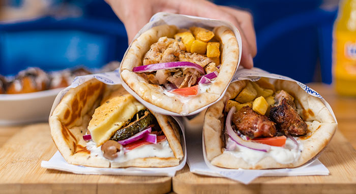 3 souvlakia sitting on serving board with hand grabbing one