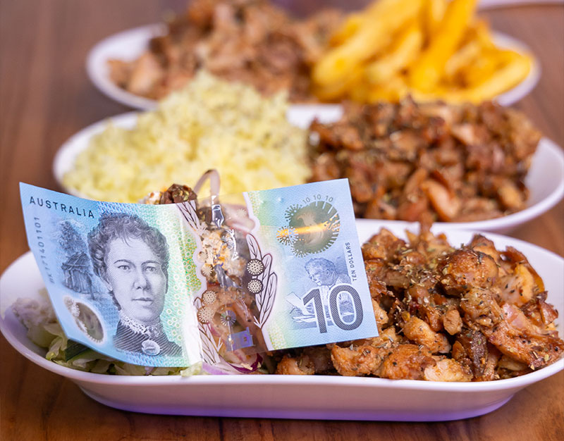 An australian $10 note sitting on top of a $10 value range meal which is made up of chicken and rice