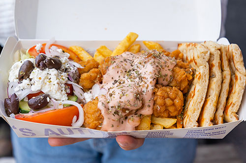 Photo of a person holding a gyro takeaway meal including chicken, Salad, Pita, Chips and Tzatziki