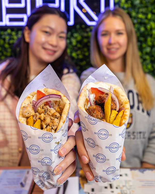 two girls next to each other holding up a souvlaki and gyro each